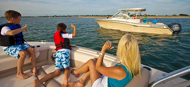 A woman and two children sitting on a boat waving at people on another boat passing by