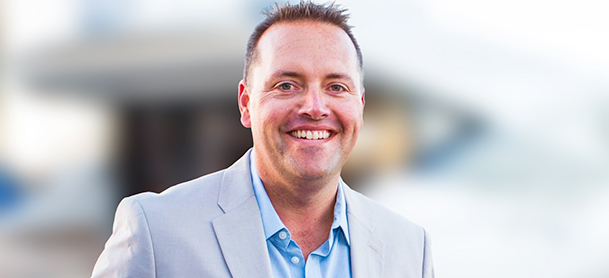 Collin Heimensen in a light gray suit and blue shirt smiles warmly.