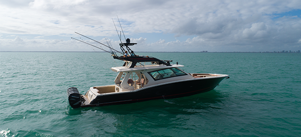 A sleek fishing boat with three outboard engines and fishing rods anchored on a calm turquoise sea under a partly cloudy sky, creating a serene atmosphere.