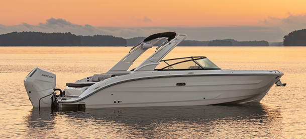 A sleek white SDX 270 OB sits on calm water at sunset.