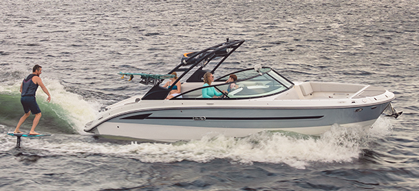 A man foil surfs on choppy waters alongside an SDX 270 Surf carrying three people.