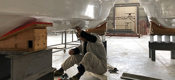 A factory worker seated on the floor working on the hull of a power catamaran