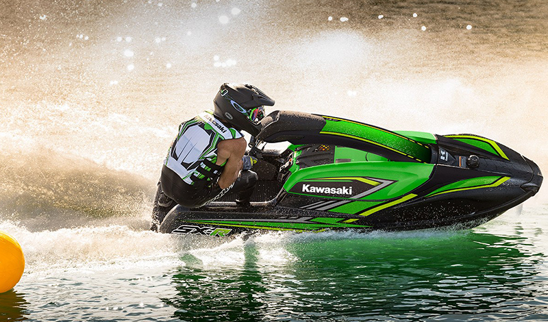 a man with a helmet and lifejacket making a turn on a green kawasaki jet ski in the water