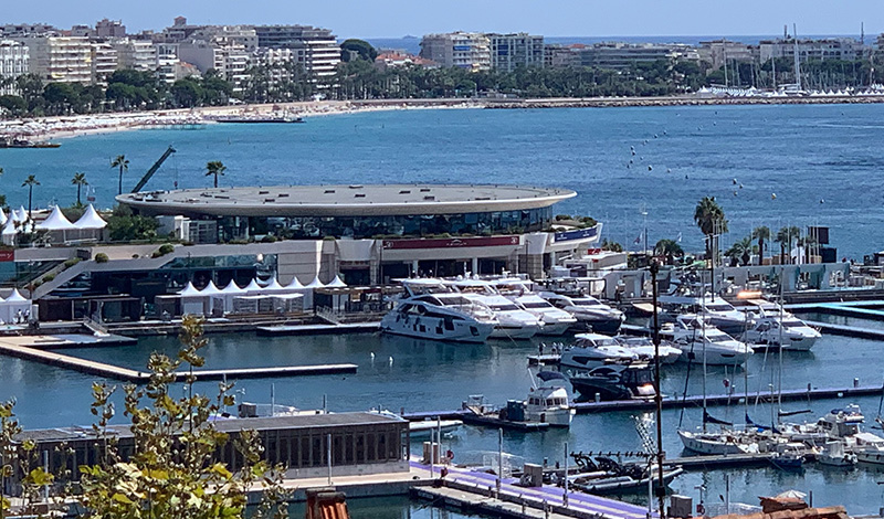 a view of numerous yachts docked at the cannes yachting festival with beaches and buildings along the water in the background