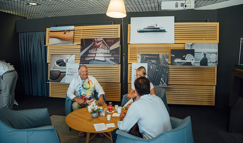 three people seated around a table at a yachting festival with photos of yachts on a wall behind them