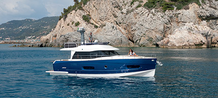 an azimut magellano 43 with a blue hull in open water with rocks and grass on the shore behind it
