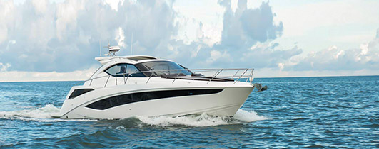 a galeon yacht with a white hull cruising through blue water from left to right