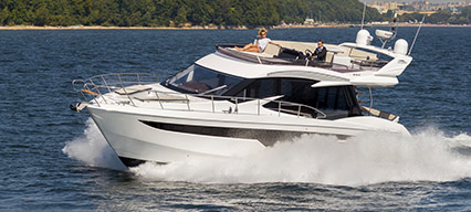 a galeon yacht with a white hull cruising through blue water from right to left