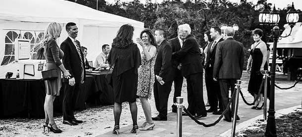Black and white image with people gathered around a table and tent with velvet ropes