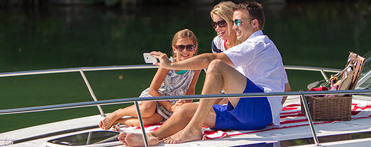 a couple with a young daughter taking a selfie on the daybed of a boat