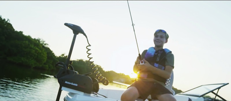 Boy fishing on boat at sunset