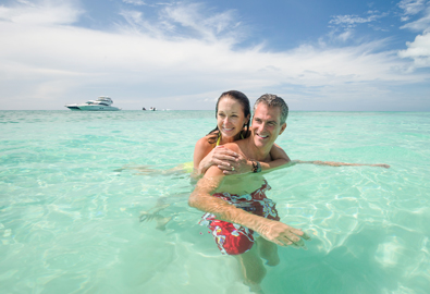 couple in clear water with yacht in background
