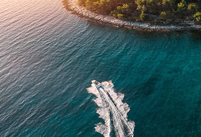 An aerial view of a boat cruising through clear blue water on a sunny day