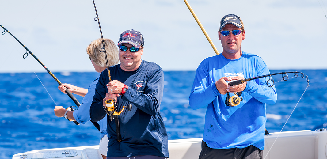 three people joyfully fishing on a boat under a clear sky with fishing rods poised over the deep blue ocean