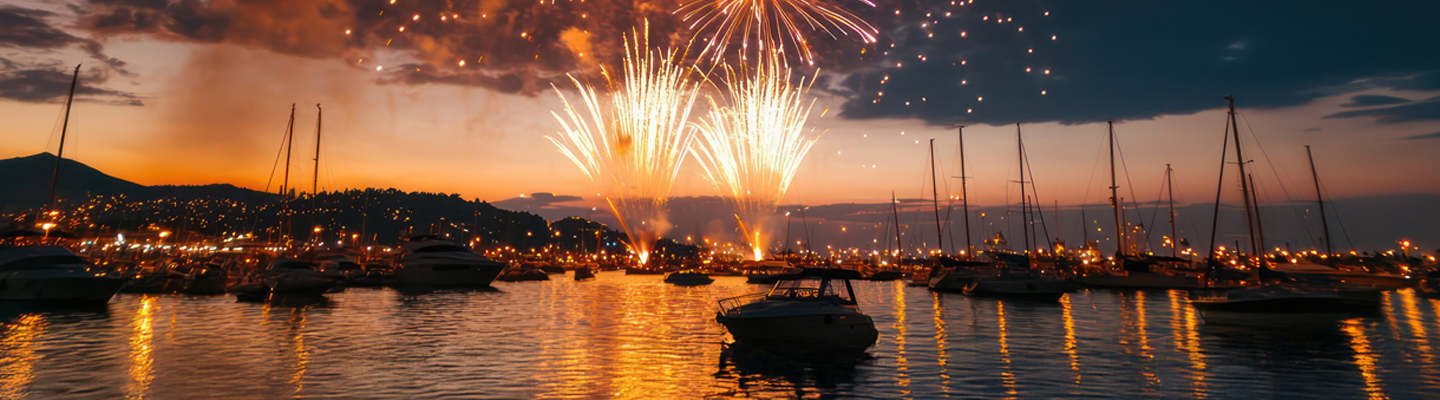 fireworks burst in vibrant orange over a marina at dusk lighting up the dark sky