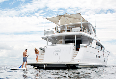 Lady laughs while watching man on long board row towards luxurious private yacht