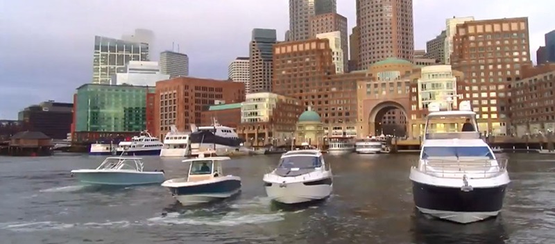 A line of four boats cruising with the Boston skyline behind them