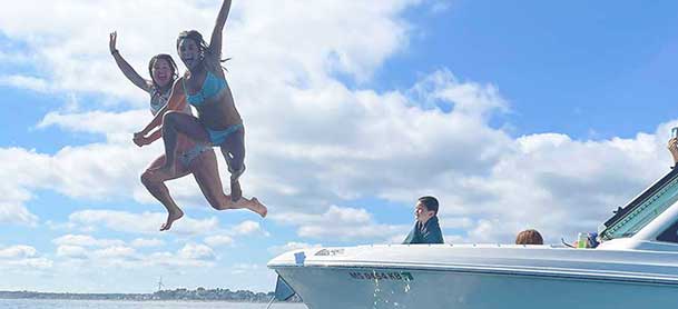 Two girls jumping off a Boston Whaler boat