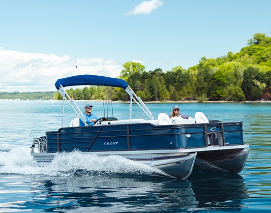 Crest pontoon in water with man driving and woman in front