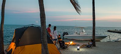 family camping sitting around a fire with boat anchored in the background