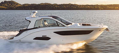 An aft cabin Sea Ray speeds across a serene lake, leaving a trail of white wake.