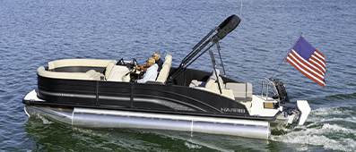 A Harris pontoon glides on a sunny, calm lake. An American flag flutters at the back.
