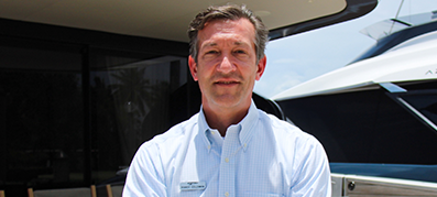 Randy Coleman stands outdoors, in front of a yacht and building.