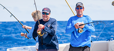 Three people joyfully fishing on a boat under a clear sky, with fishing rods poised over the deep blue ocean.