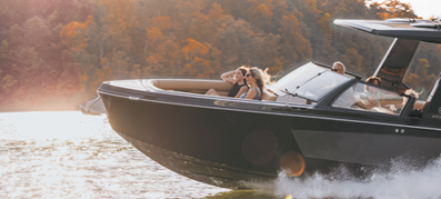 An Aviara speeds across a sunlit lake, creating white waves. Onboard, two women enjoy the ride, surrounded by autumnal trees.