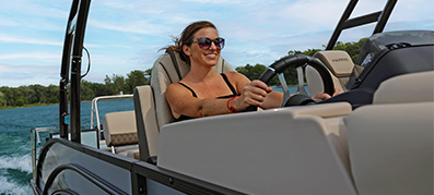 Woman smiling and steering a pontoon on a sunny day.