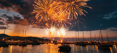 Fireworks burst in vibrant orange over a marina at dusk, lighting up the dark sky.