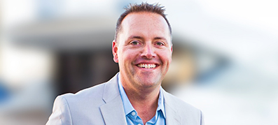 Collin Heimensen in a light gray suit and blue shirt smiles warmly.