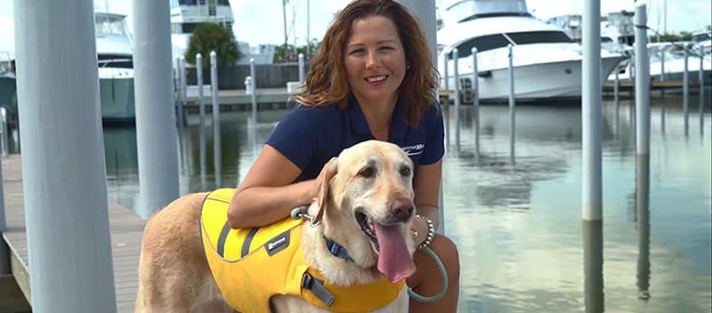 woman squatting next to dog in yellow lifejacket