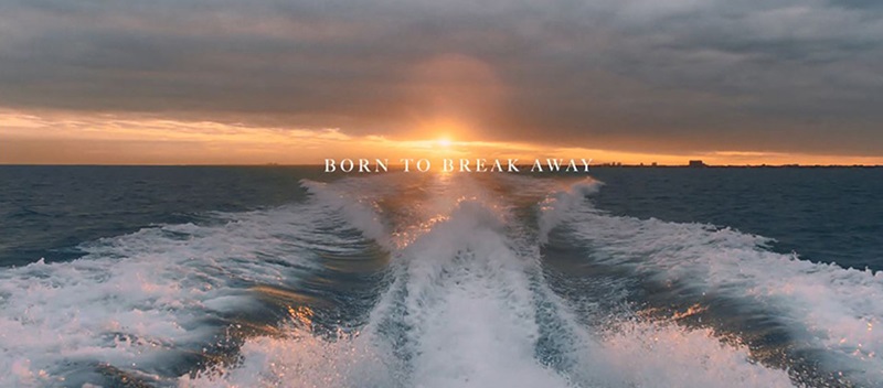A view off a boat's wake with the sunset behind it, and the words born to break away on the horizon