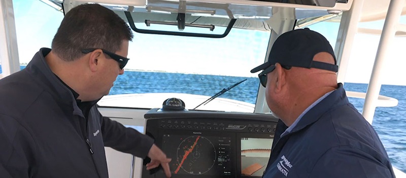 Two men looking at the navigation screen on a boat, as it shows a red diagonal line across the middle.