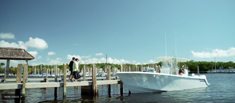 Two men walking along a dock towards their yacht with fishing gear