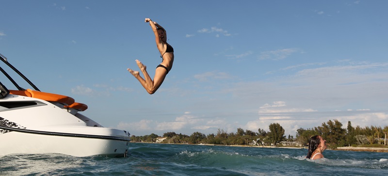 Women excitedly jump off a yacht into the blue water