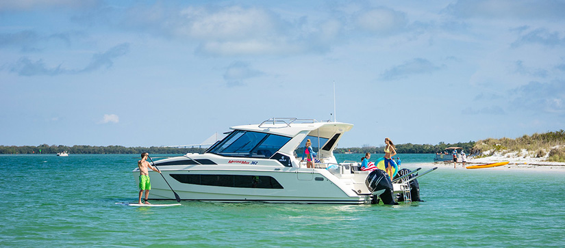 boat anchored near beach, a man on a paddle board and a lady and a small kid by the beach