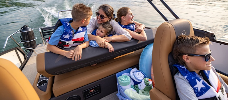 A smiling family with life vests enjoys a ride on a Harris pontoon.