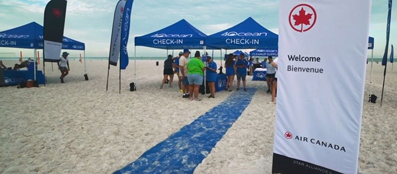 A blue carpet on a beach leading to a blue tent with 4ocean's logo on it, and people standing at a table underneath