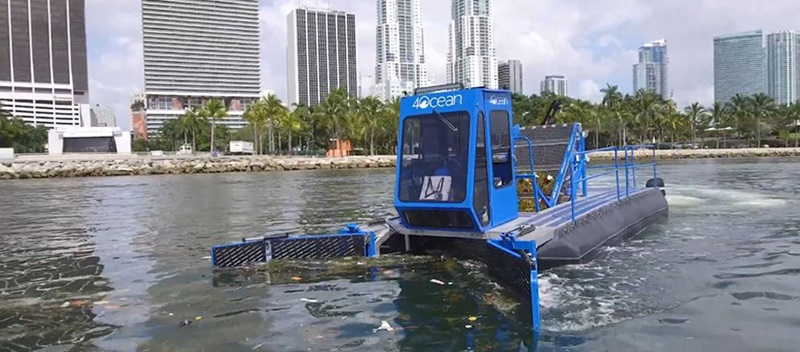A blue vessel with the 4ocean logo on it, cruising the water and skimming up trash on the surface
