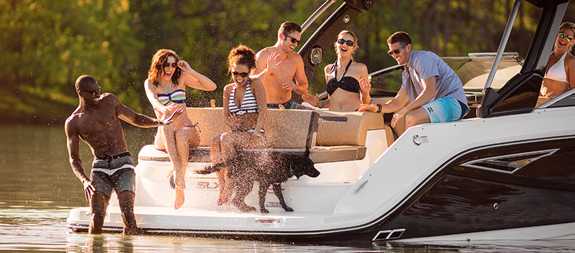 A group of friends and a dog enjoy a sunny day on a boat, laughing and splashing water, conveying a joyful and relaxed summer vibe.