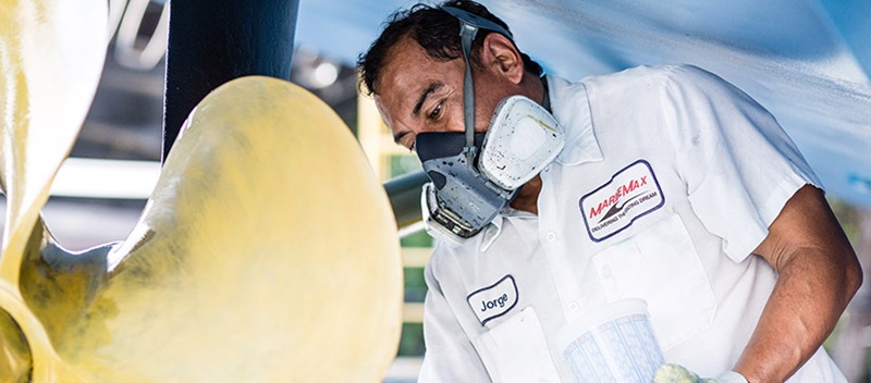 A man with a breathing mask and a white MarineMax shirt working on the motor on a boat
