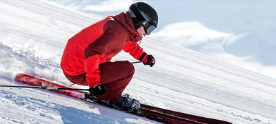 man in red jacket and black helmet racing down a ski hill on red skiis
