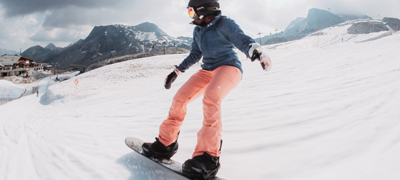 young woman snowboarding on a wide ski slope with mountains in the background