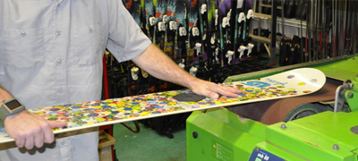 a trained professional ski shop technician prepares a snowboard base for wax application