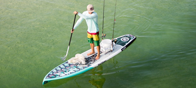 man paddling while standing on a stand up paddle board with two fishing poles resting on the back