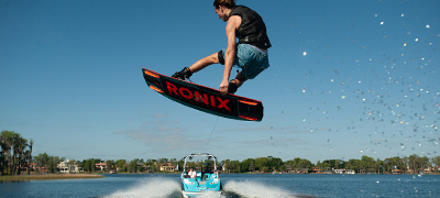 woman catching big air on a red and balck ronix wakeboard behind a reef blue nautique super air 230