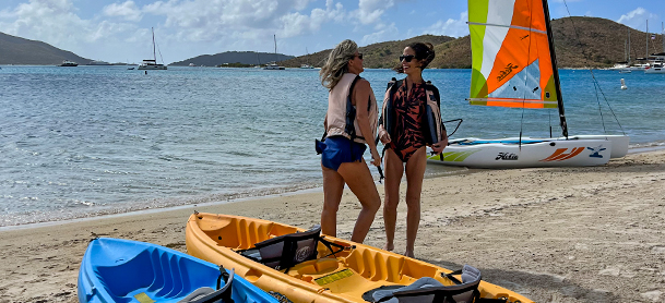 blue and orange kayaks on the beach with two people next to them