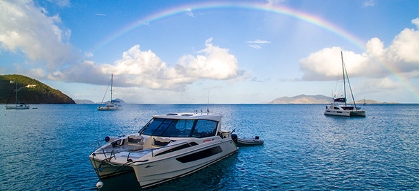 An Aquila power catamaran in the water under a rainbow in the sky